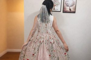 Kvinna bakifrån i en broderad brudslöja och ljusrosa klänning, som en presentidé.