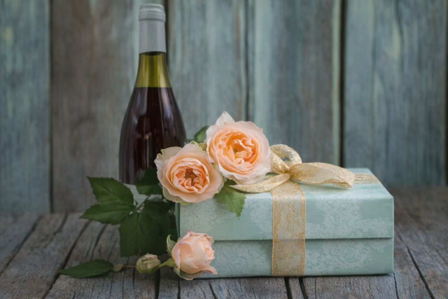 En vinflaska, inpackat paket och rosor på träbakgrund, romantisk present.