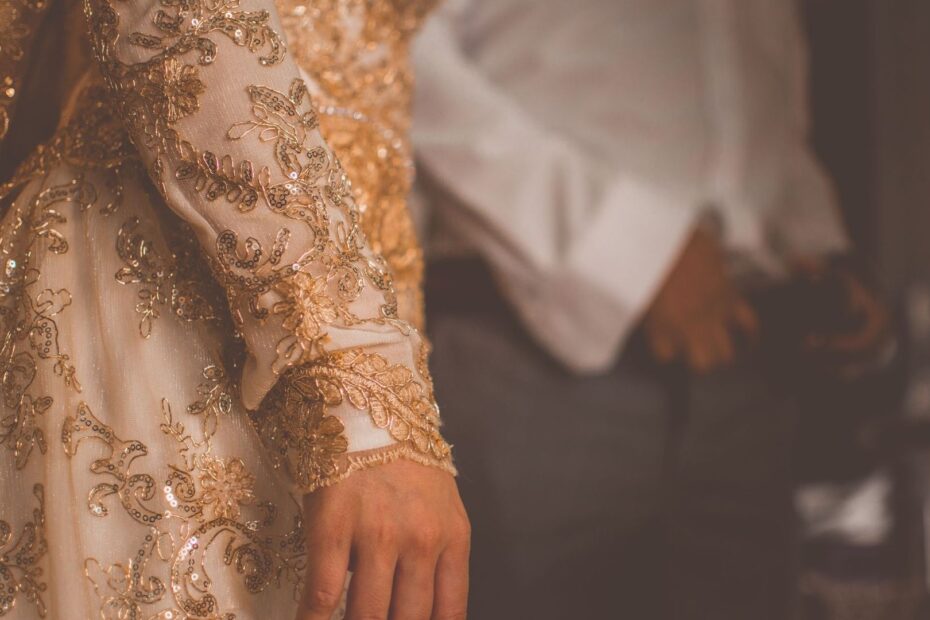 Närbild av en rikt broderad vit klänningsärm i varmt ljus